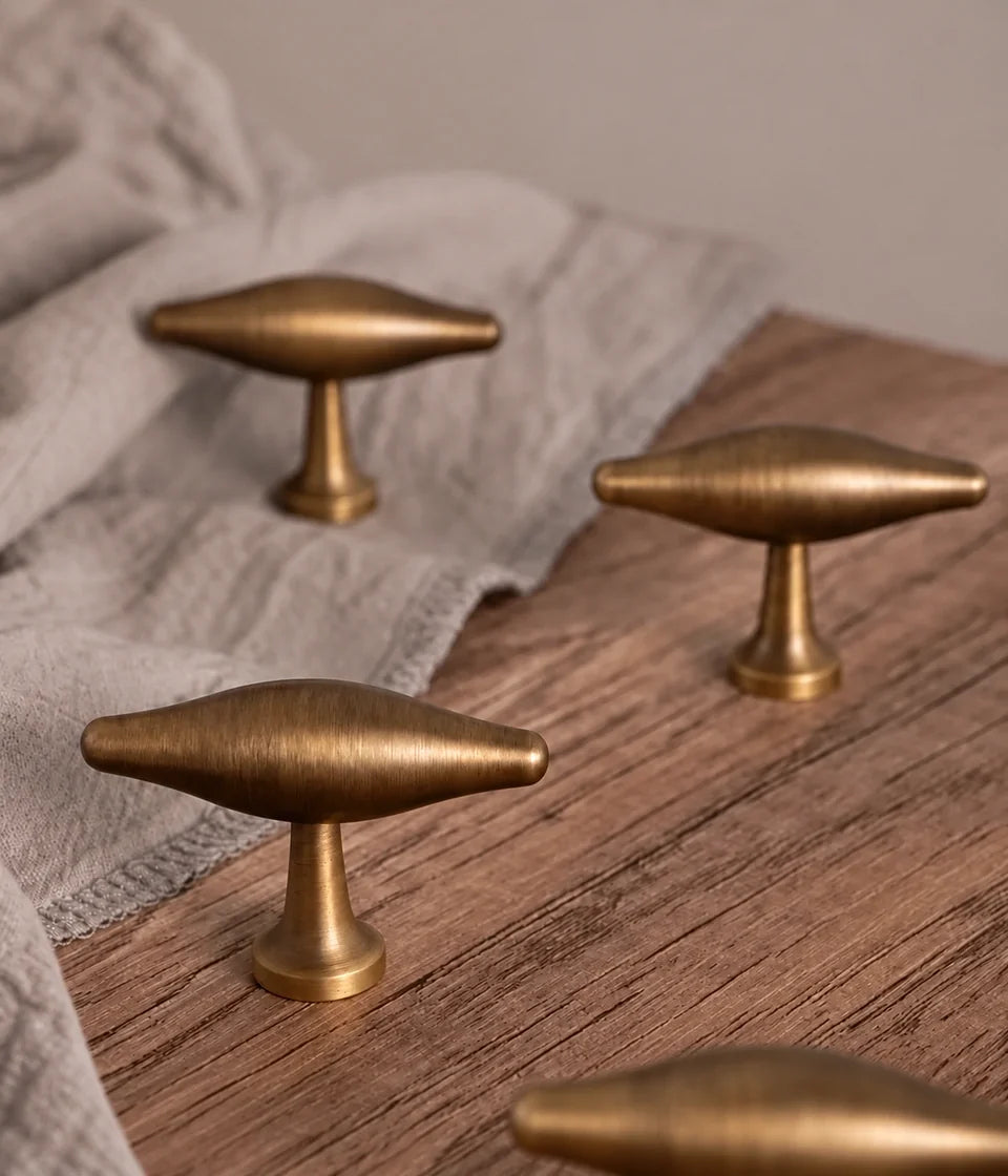 Solid brass arched cabinet pulls and oval T-knob in antique brushed brass on natural linen and wood