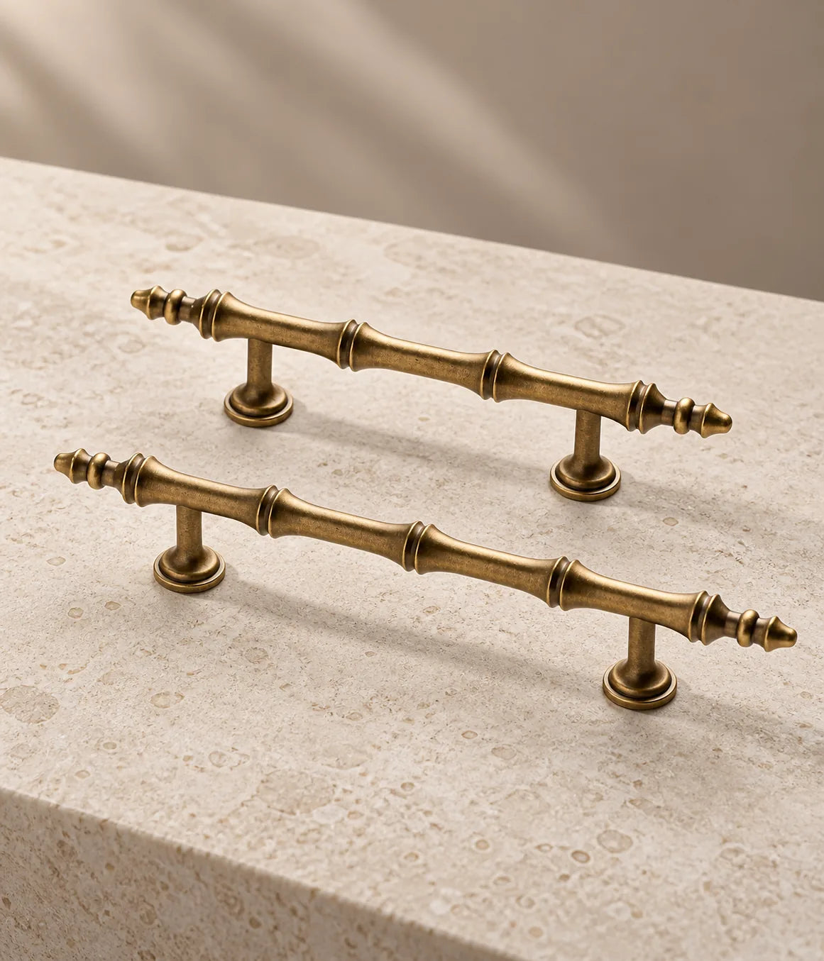 Two antique brass segmented-finial pull sizes resting on pale limestone
