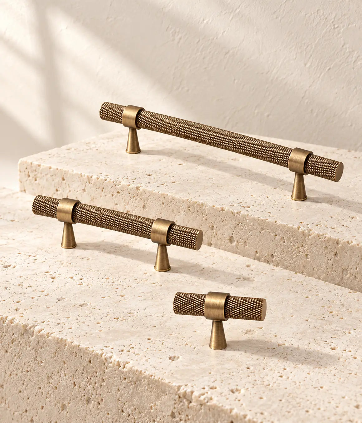 Antique brass slim-post knurled pulls and T-knob arranged on ivory limestone