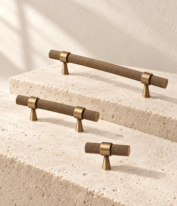 Antique brass slim-post knurled pulls and T-knob arranged on ivory limestone