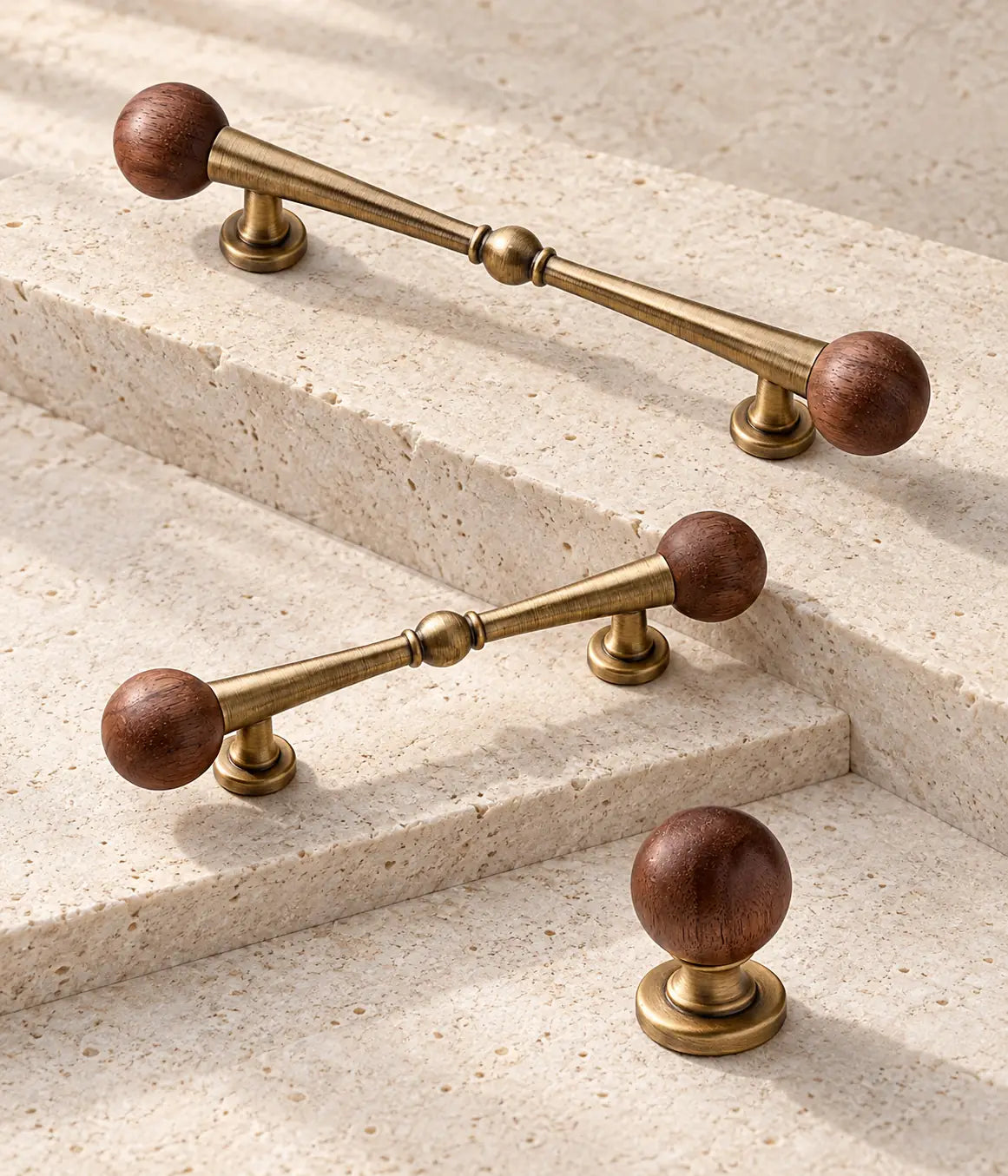 Walnut ball-end antique brass pulls and matching round cabinet knob arranged on pale limestone