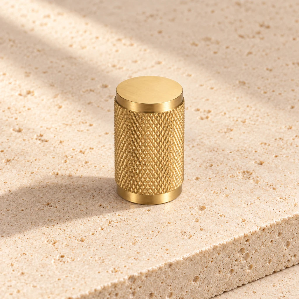 gold brass cross knurled cylinder knob on pale limestone.
