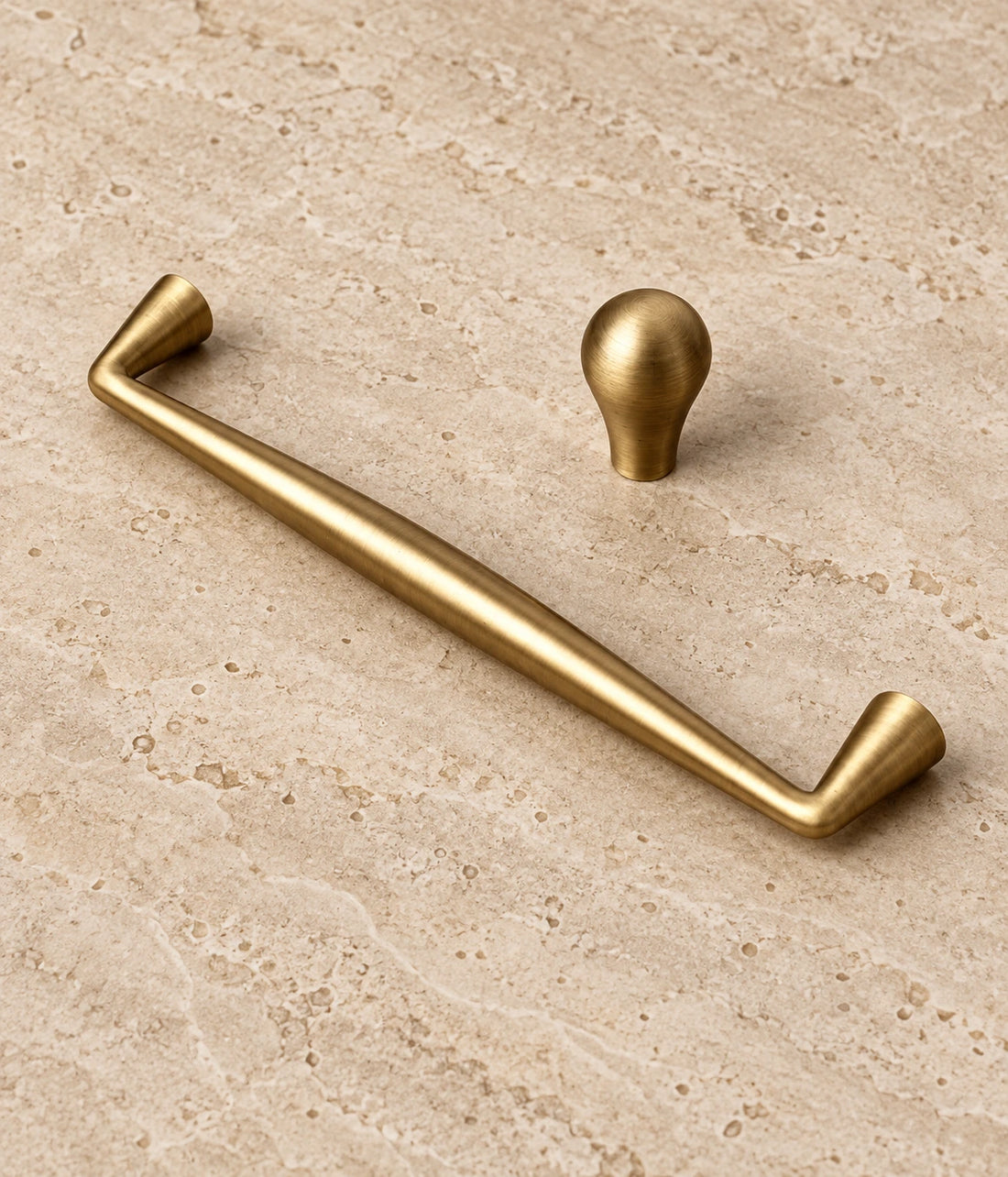 Antique Brass Tapered Cabinet Pulls & Teardrop Knob arranged on warm limestone, showing the antique brushed brass finish