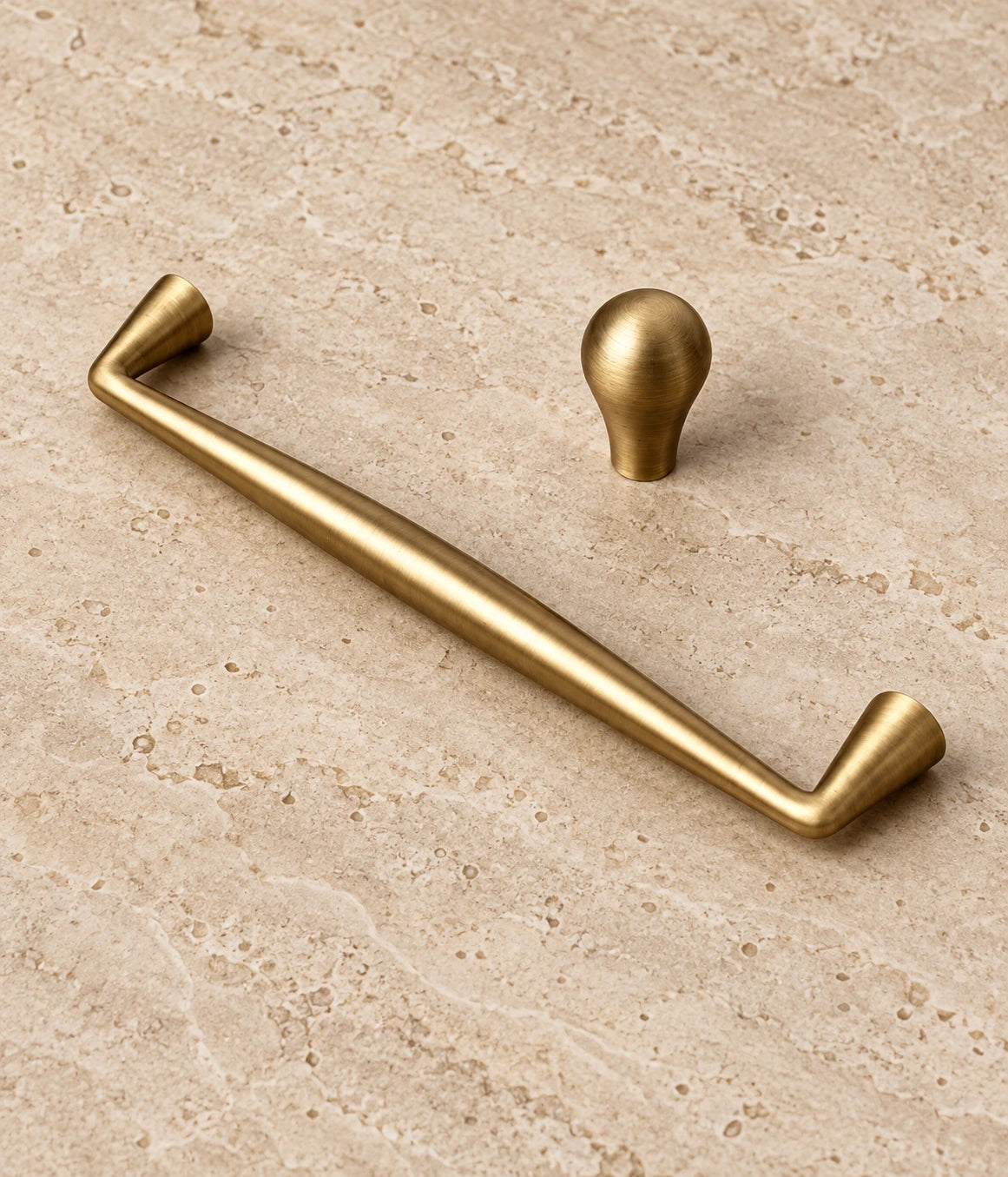 Antique Brass Tapered Cabinet Pulls & Teardrop Knob arranged on warm limestone, showing the antique brushed brass finish