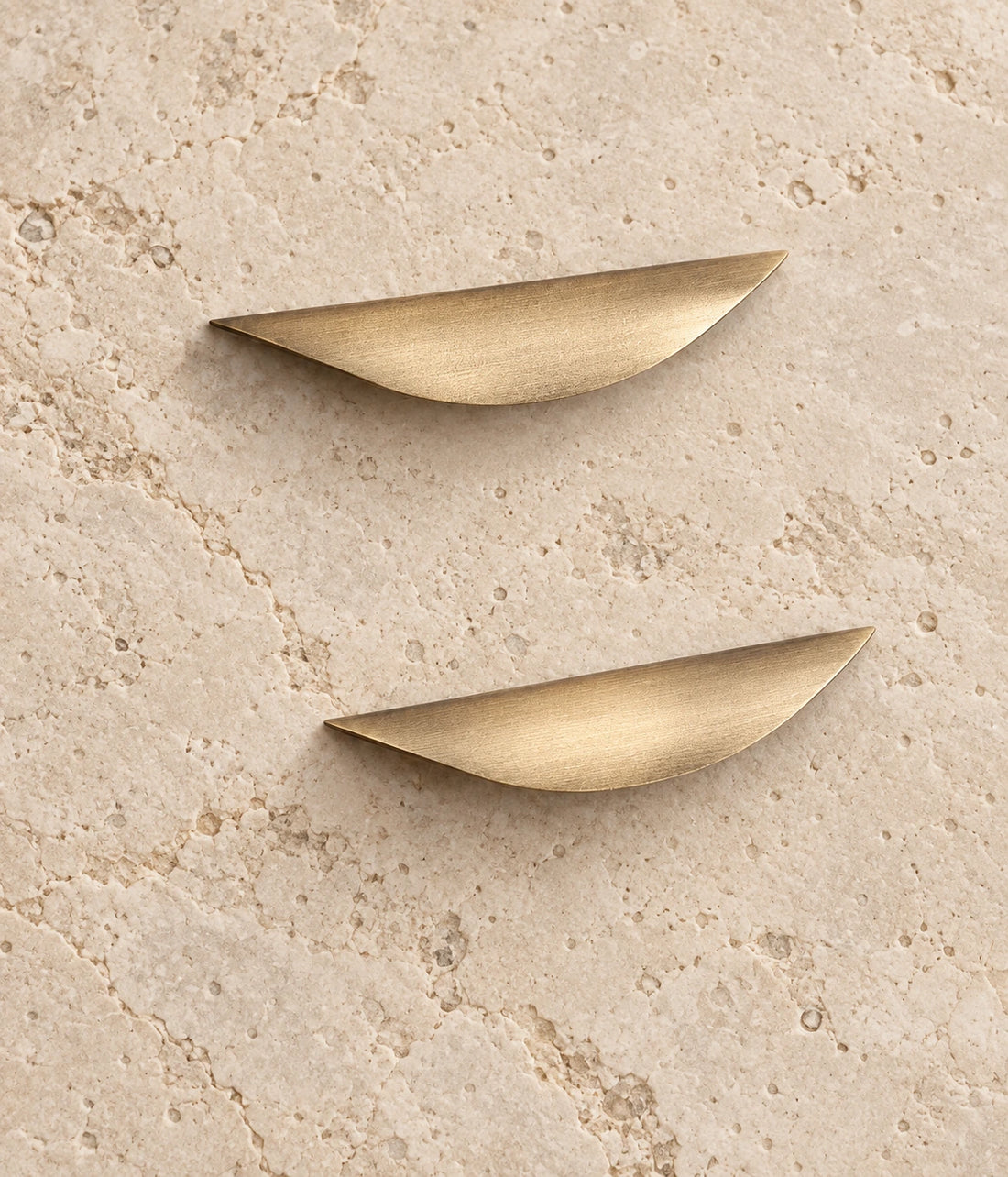 Antique Brass Crescent Cabinet Pulls on warm limestone, showing the antique brushed brass finish