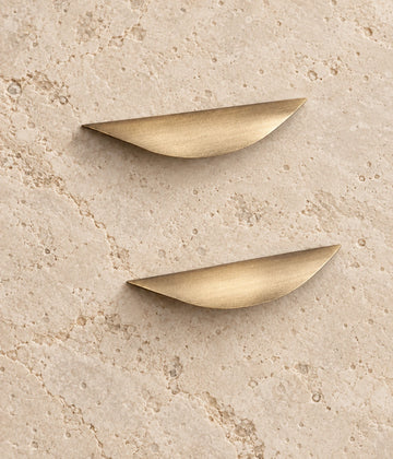 Antique Brass Crescent Cabinet Pulls on warm limestone, showing the antique brushed brass finish