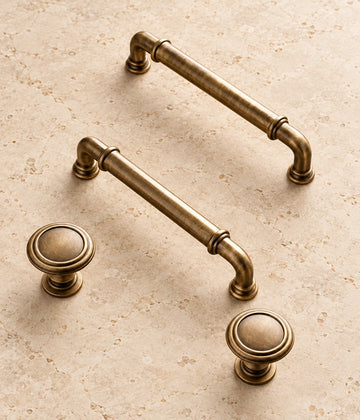 Antique Brass Collared Cabinet Pulls & Knob on warm limestone, showing the antique brushed brass finish
