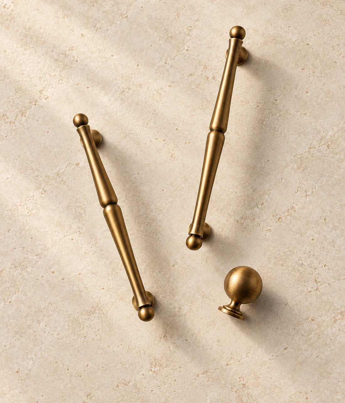 Antique Brass Turned Cabinet Pulls & Ball Knob arranged on pale limestone, showing the brushed brass finish and hardware details
