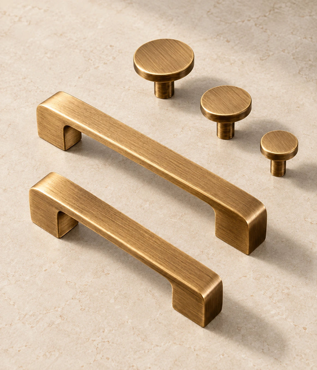 Antique Brass Flat Cabinet Pulls & Disk Knobs arranged on pale limestone, showing the brushed brass finish and hardware details