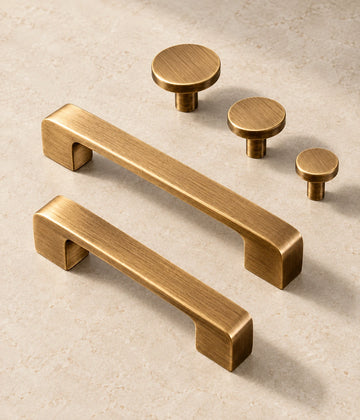 Antique Brass Flat Cabinet Pulls & Disk Knobs arranged on pale limestone, showing the brushed brass finish and hardware details