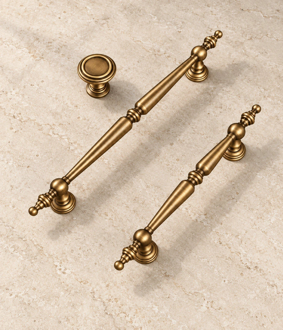 Antique Brass Finial Cabinet Pulls, Pendant Pulls & Knob arranged on pale limestone, showing the brushed brass finish and hardware details