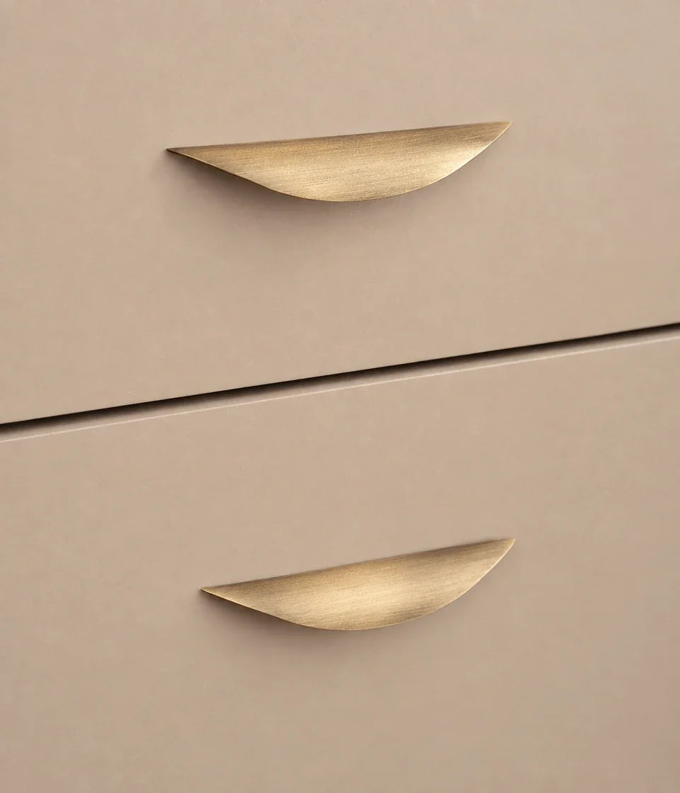 Antique brushed brass crescent pulls installed horizontally on beige drawers
