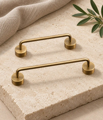 Antique brass bridge cabinet pulls with thick round bases arranged on warm ivory limestone