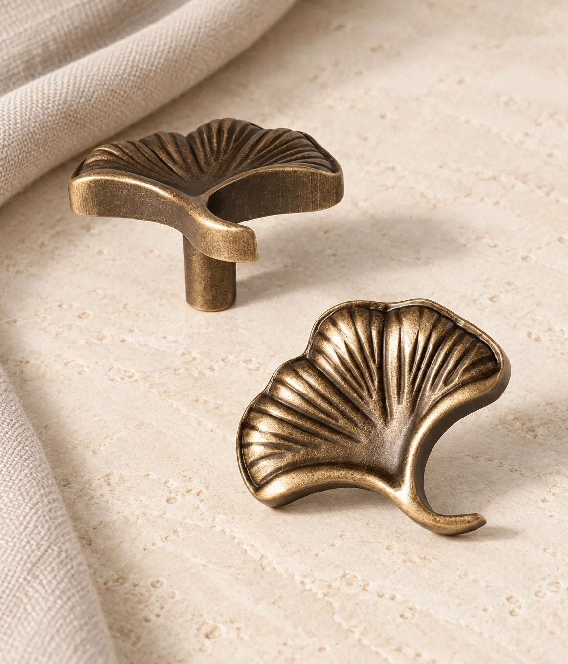 Antique brass ginkgo leaf cabinet knob shown in two views on limestone