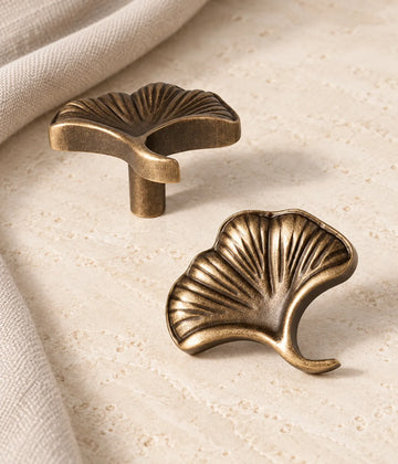 Antique brass ginkgo leaf cabinet knob shown in two views on limestone