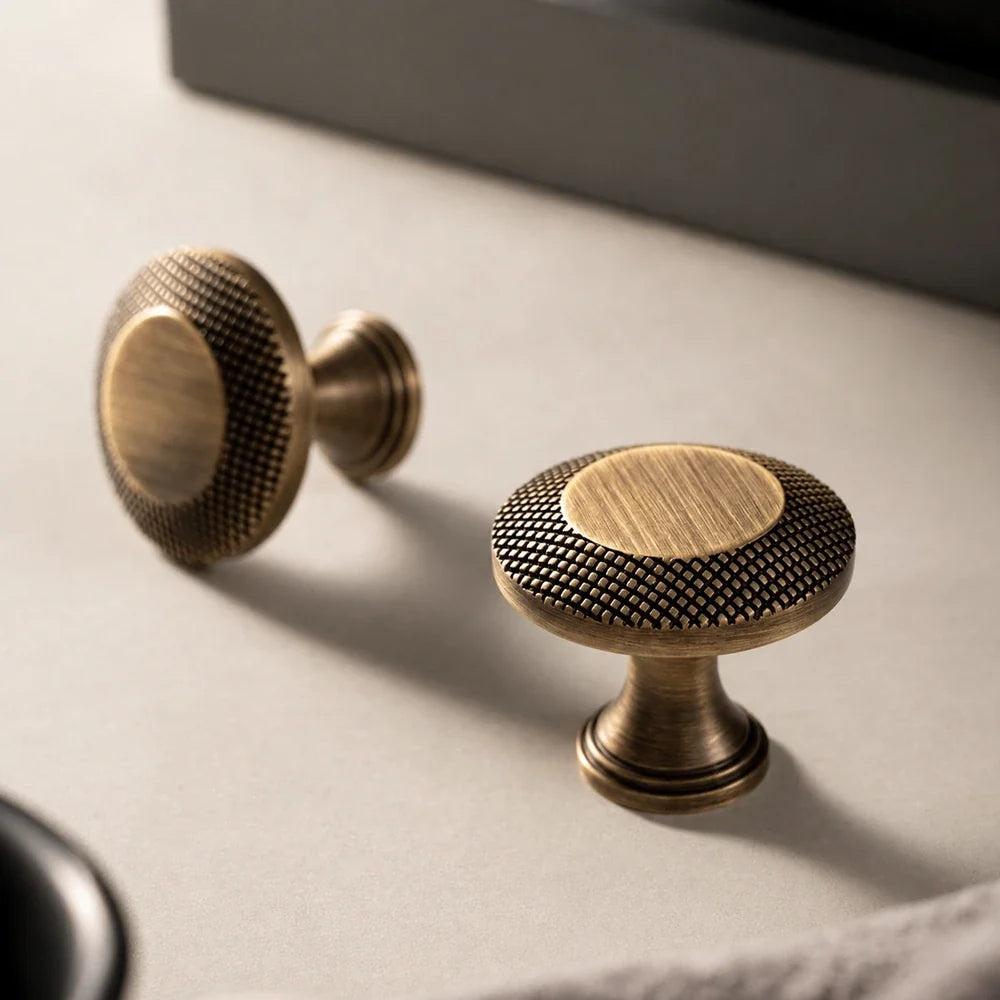 Antique brass cabinet knobs with knurled rims on a beige surface