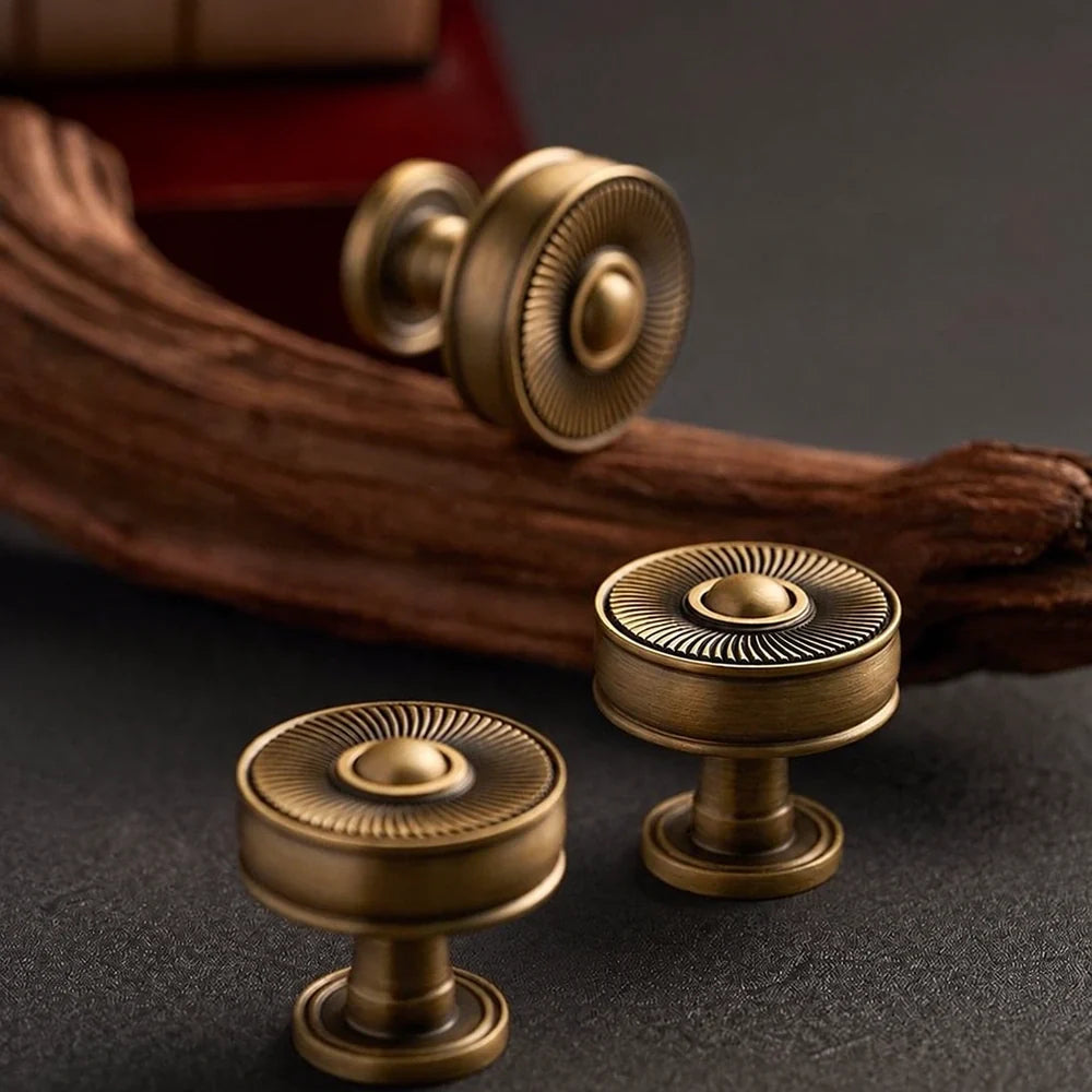 Antique brass sunburst cabinet knobs on a dark surface with driftwood
