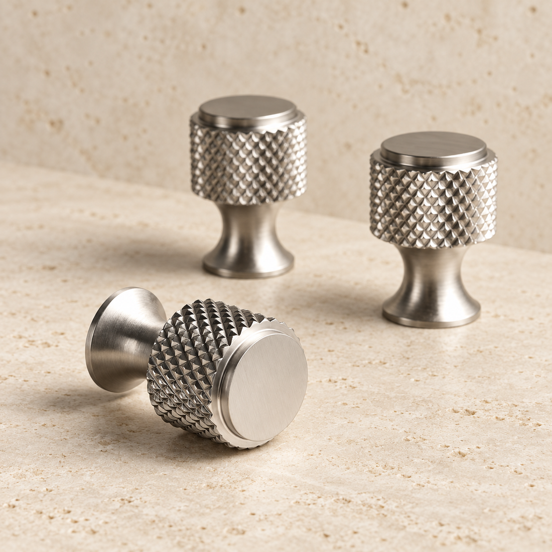 Brushed nickel diamond-knurled cabinet knobs arranged on pale limestone.