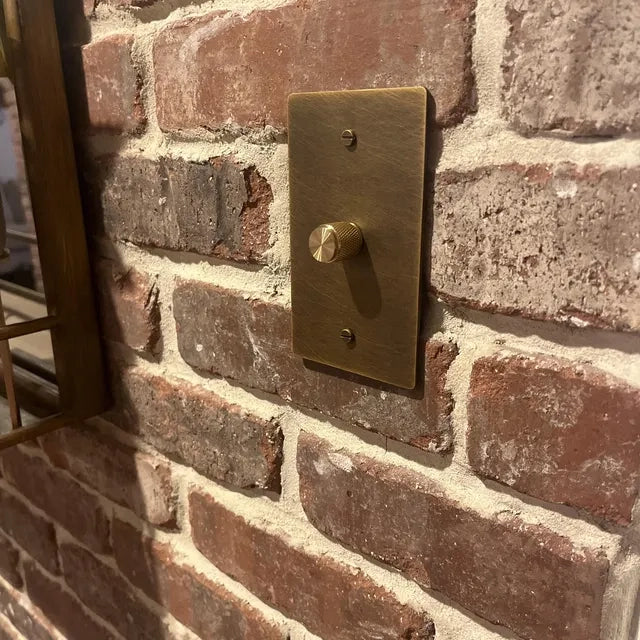 Brass rotary dimmer installed on an exposed brick wall.