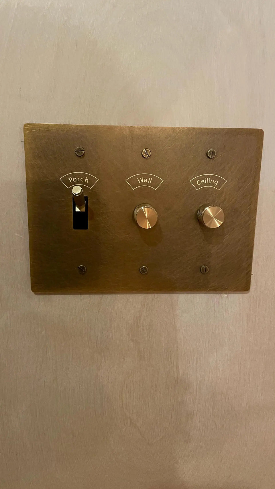 Engraved brass wall plate with one toggle and two rotary dimmers on a neutral wall.