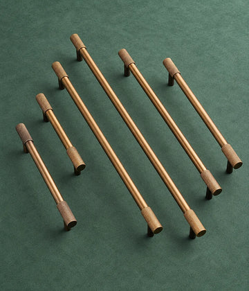 Six antique brass knurled end cabinet bar pulls on green fabric