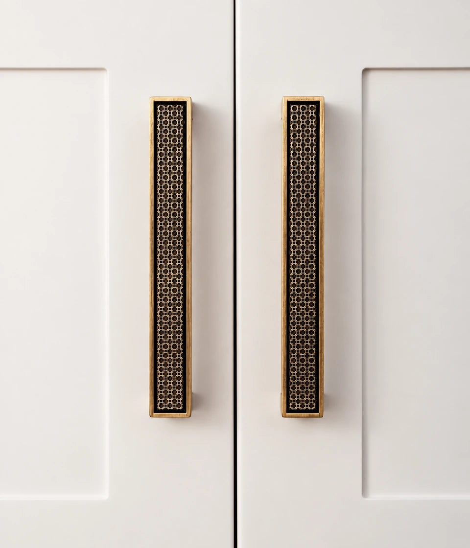 Two antique brass lattice bar pulls installed on white cabinet doors