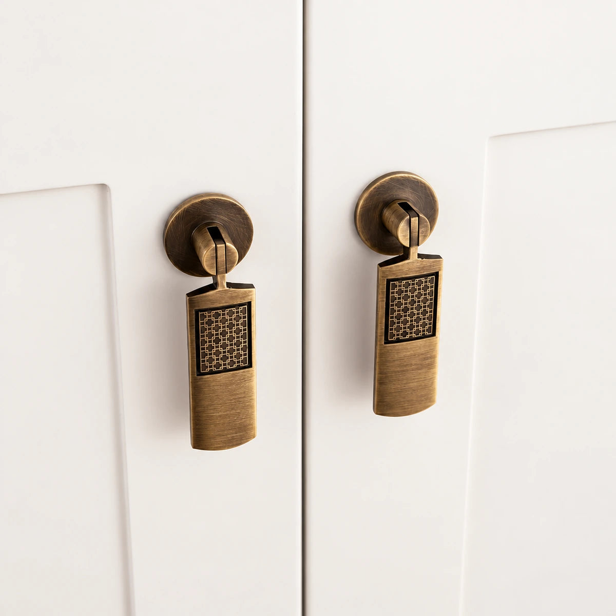 Hinged antique brass lattice pendant pulls on white cabinet doors