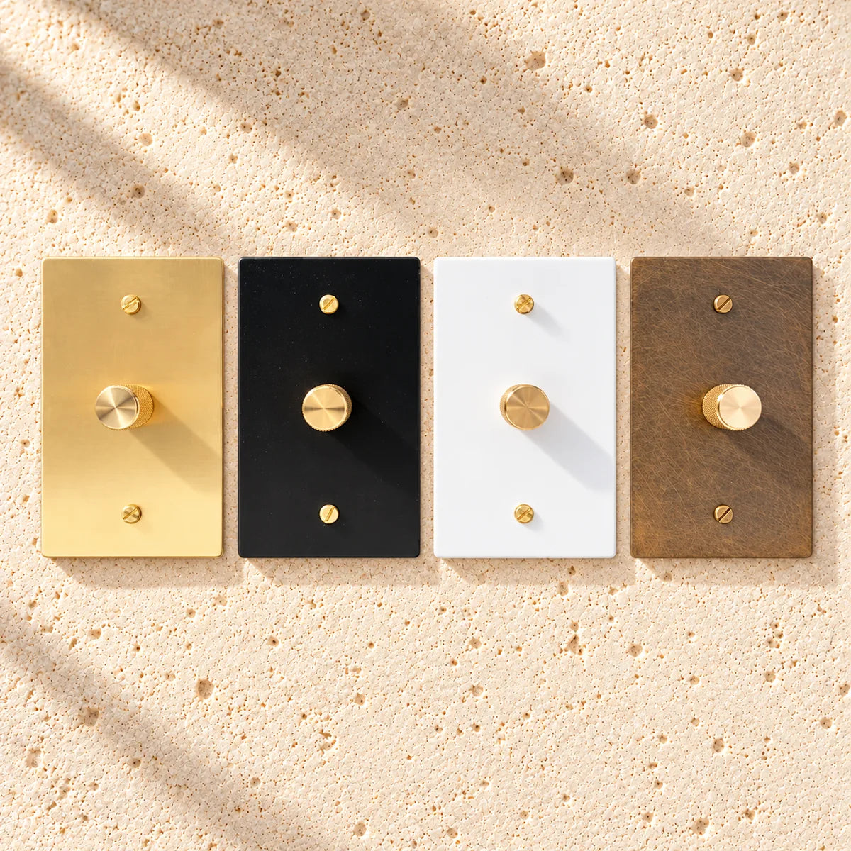 Four rectangular light switch covers in gold, black, white, and bronze on a white background.