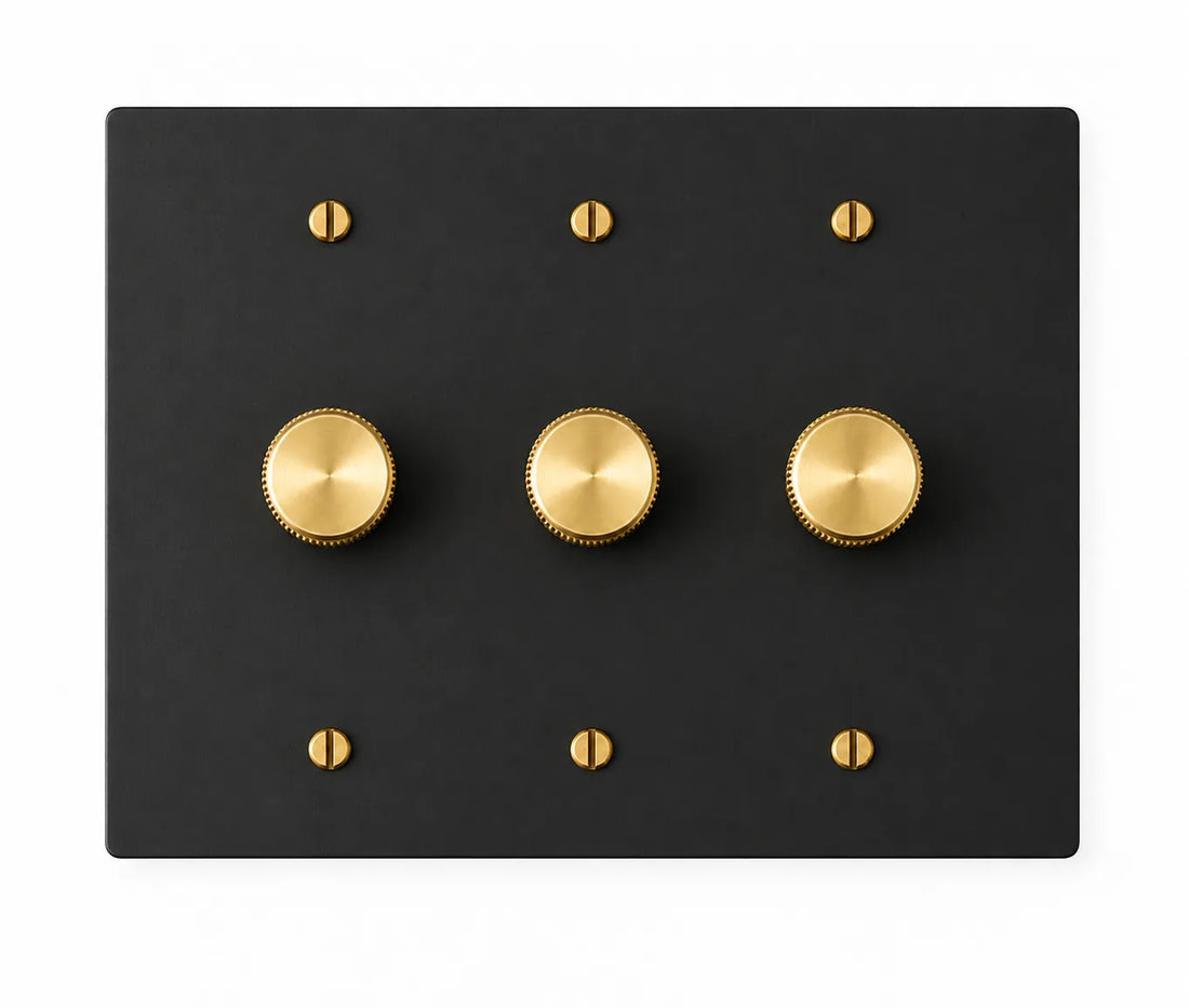 Black three-gang plate with three brass rotary dimmer knobs and six brass screws