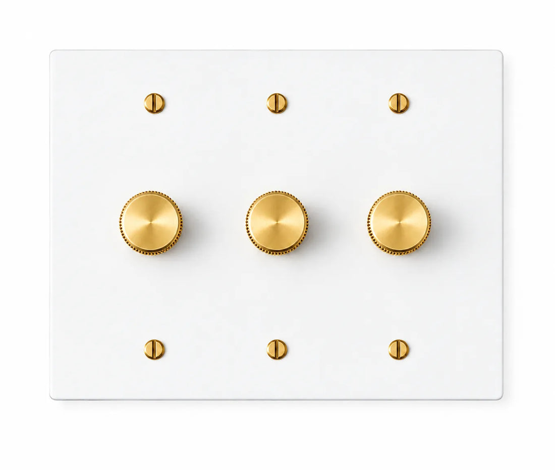 White three-gang plate with three brass rotary dimmer knobs and six brass screws