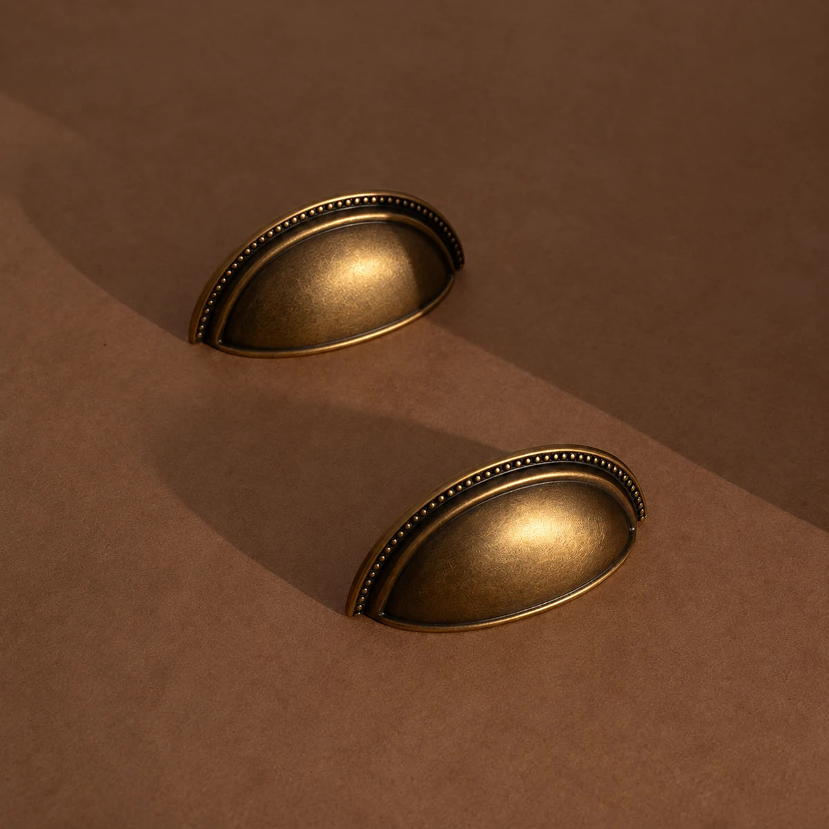 Two deep beaded antique brass cup pulls on a brown background