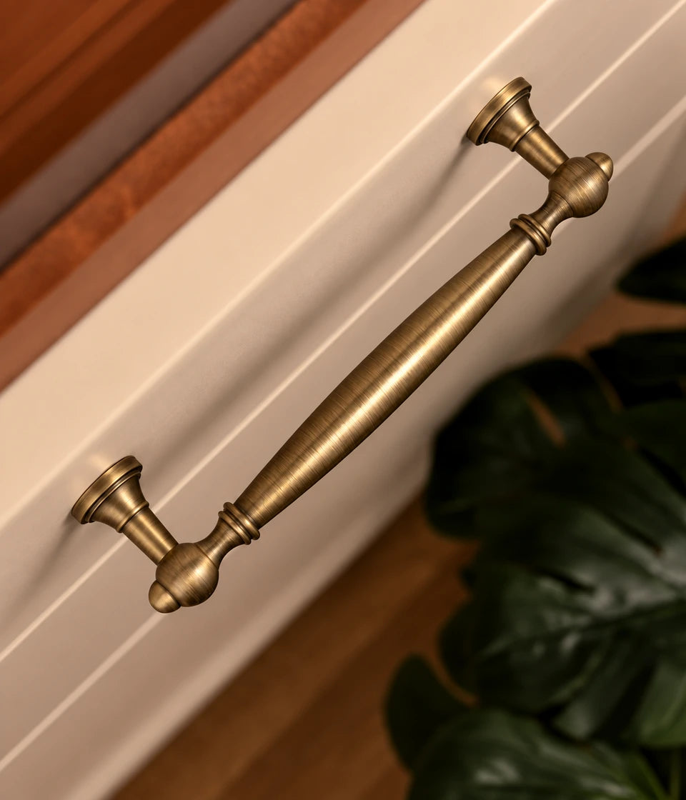 Antique brass smooth spindle cabinet pull installed on a cream cabinet