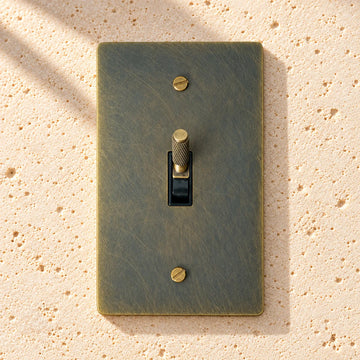 1-gang aged bronze knurled toggle light switch on pale limestone