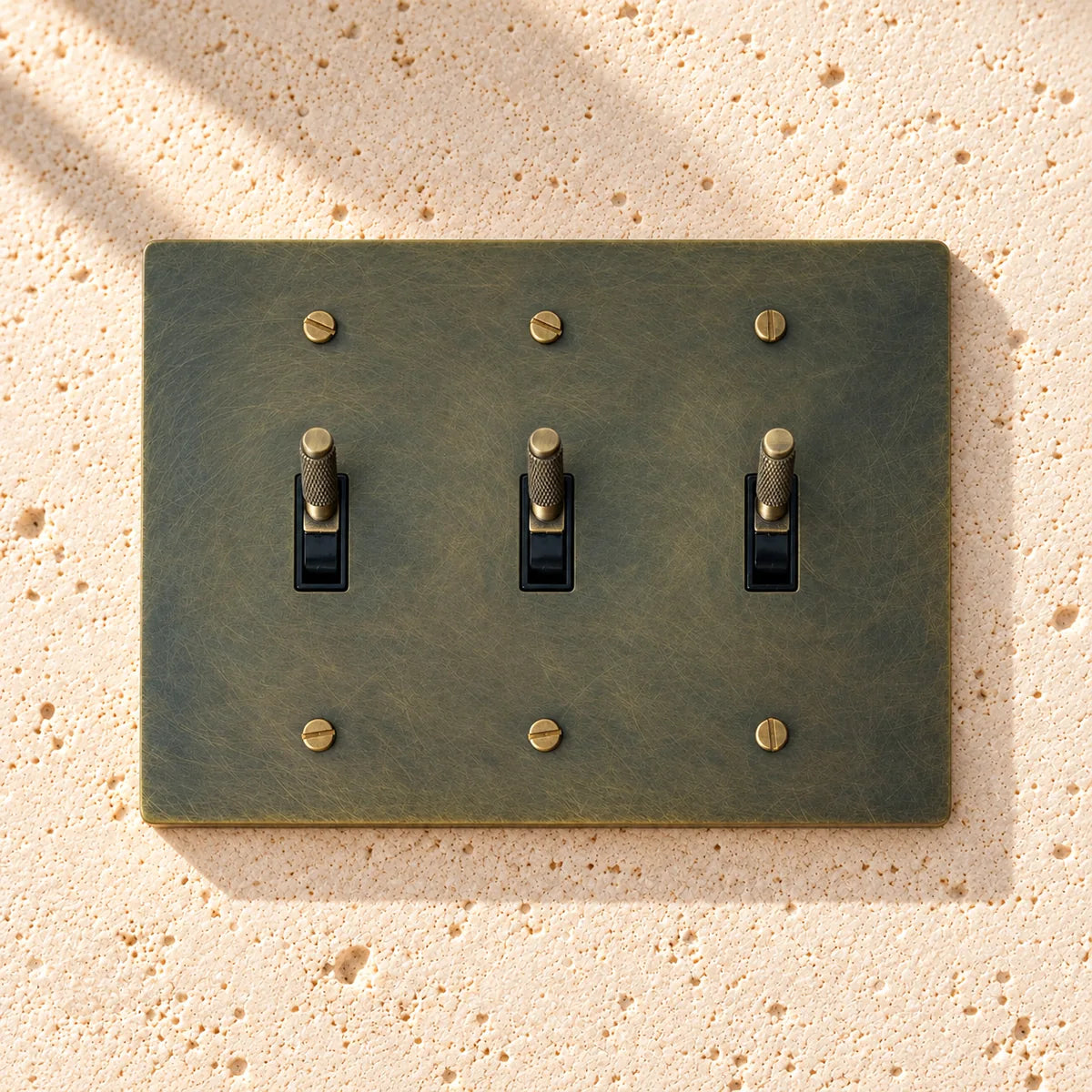 3-Gang Solid Brass Knurled Toggle Light Switch on sunlit pale limestone