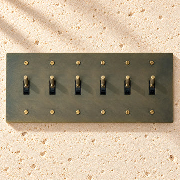 6-Gang Solid Brass Knurled Toggle Light Switch on sunlit pale limestone