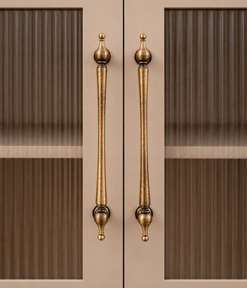 Long antique brass urn-finial cabinet pulls installed on glass-panel doors