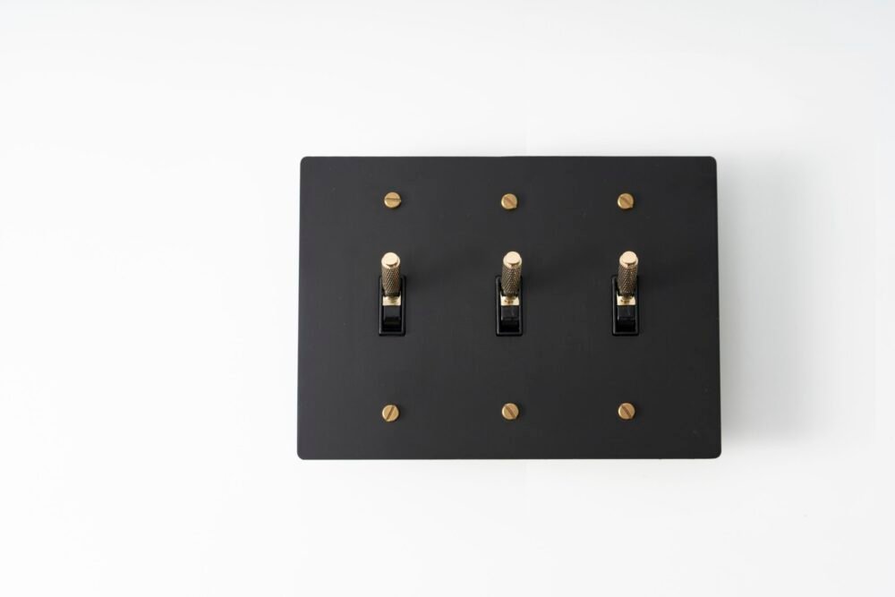 Three-Gang Black Brass Plate with Golden Knurled Toggle Switch - Sophisticated triple-toggle switch in a black brass finish, featuring elegant golden knurled accents.